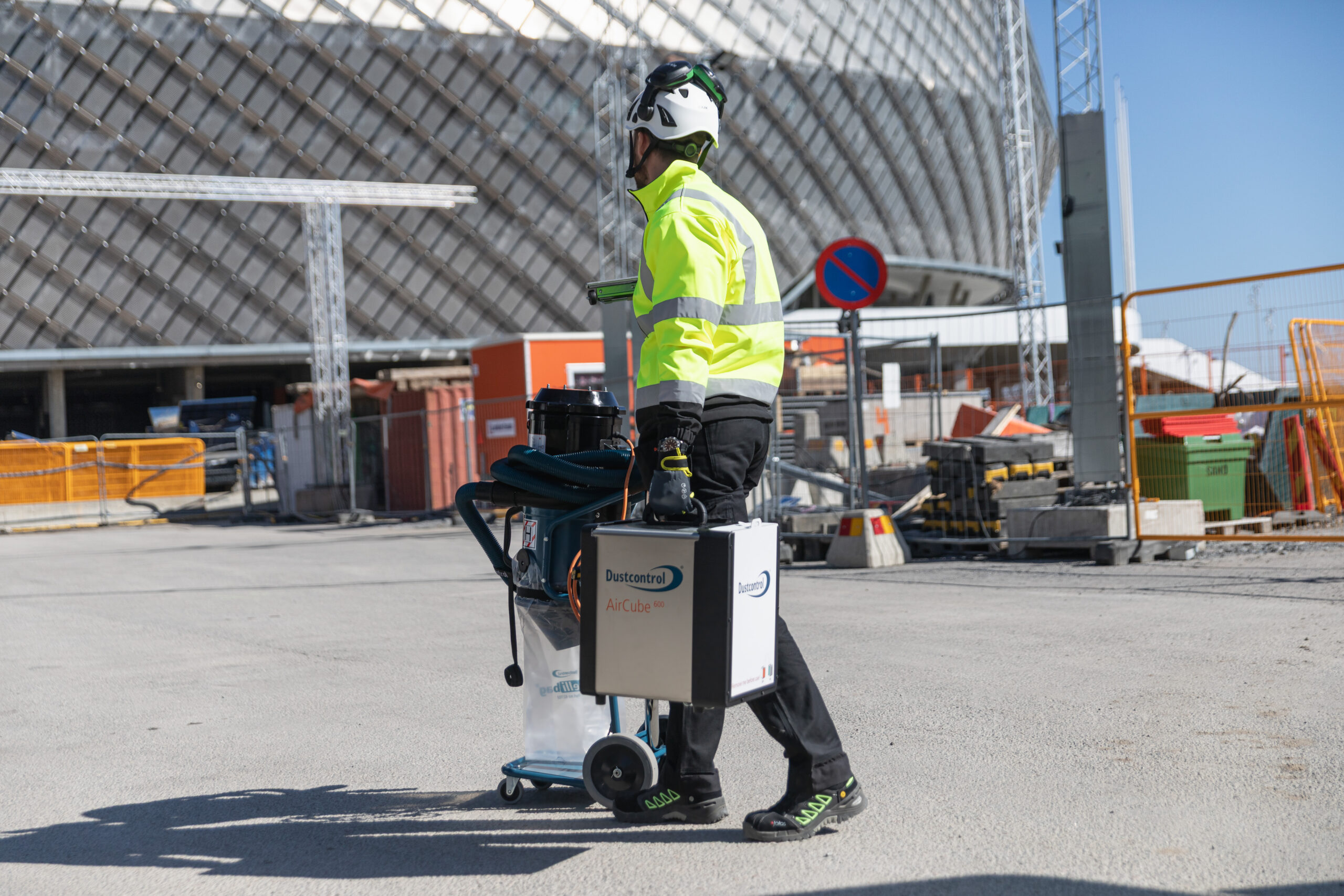 En arbetare som bär en luftrenare och skjuter en stoftavskiljare (byggdammsugare, industridammsugare) framför sig.
